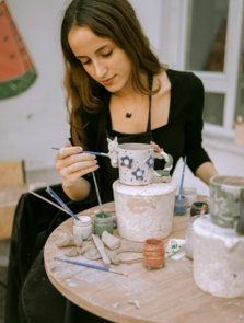 a woman sitting at a table painting a cake